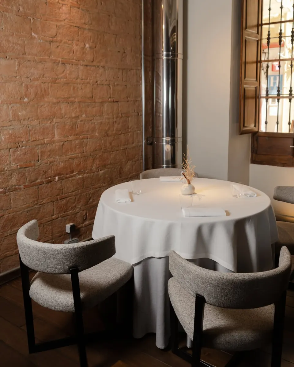 Una mesa redonda junto a la pared de ladrillo visto y una ventana alta