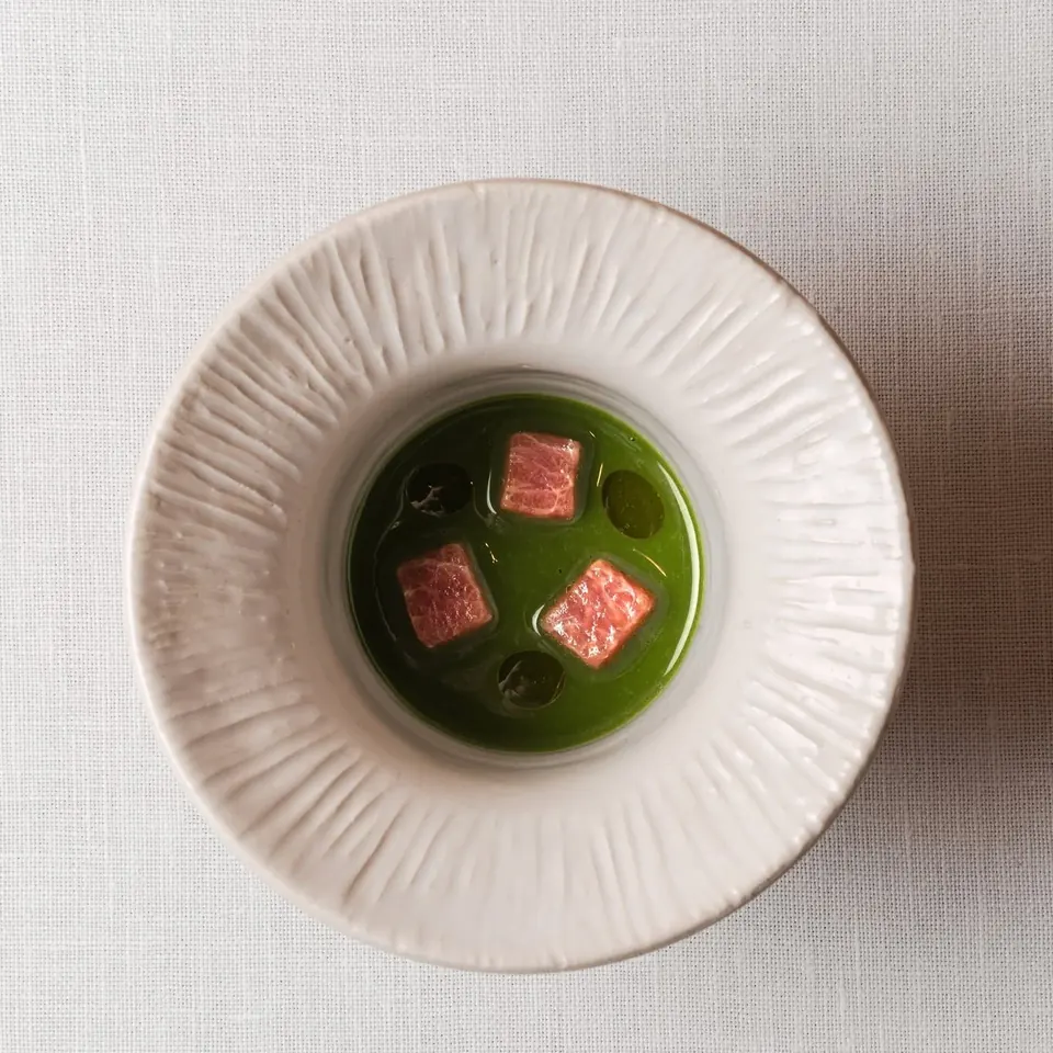 Vista cenital de un caldo verde con dados rosados en un plato de cerámica blanca
