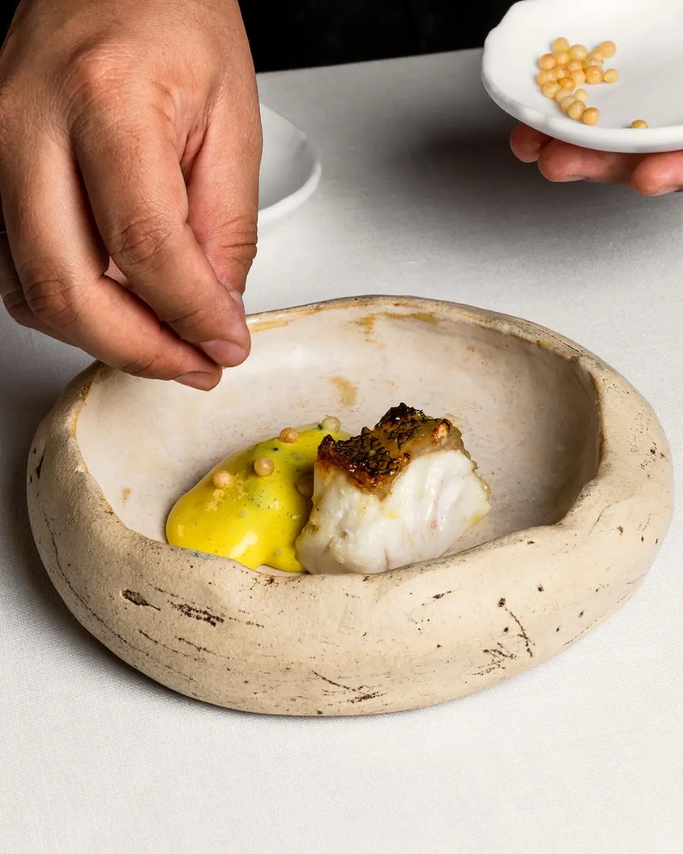 Una mano termina un plato de pescado con salsa amarilla