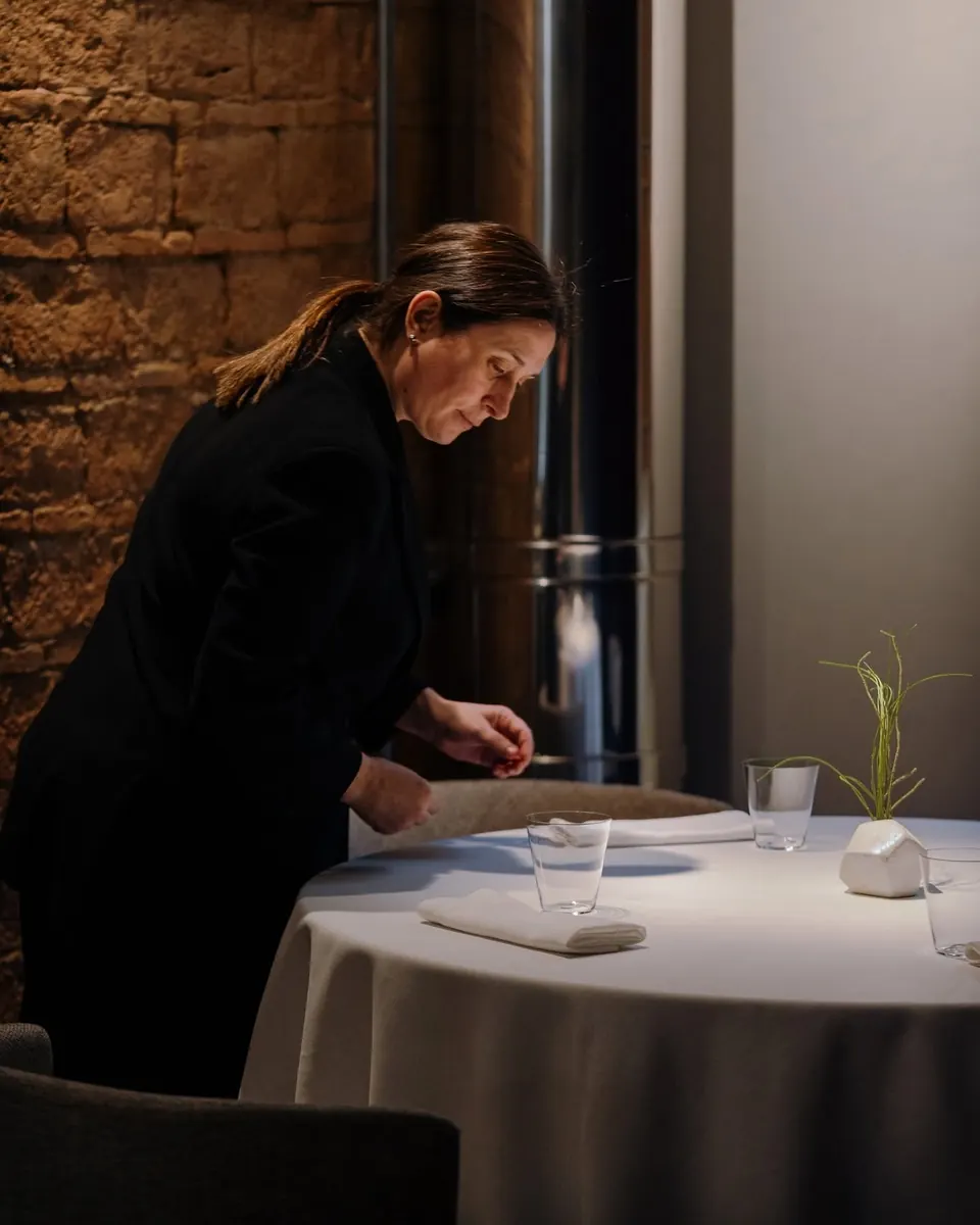 Una camarera prepara una mesa junto a la pared de ladrillo